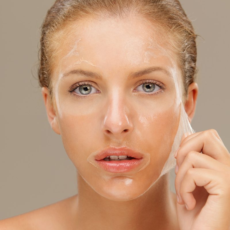 closeup beauty portrait of beautiful blonde woman peeling off a facial mask